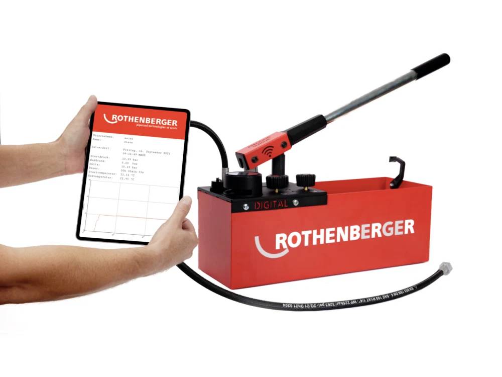 Digitale Druckprüfpumpe von Rothenberger, mit angeschlossenem Tablet zur Anzeige der Testergebnisse. Rote Pumpe mit manueller Kurbel und Schlauch.