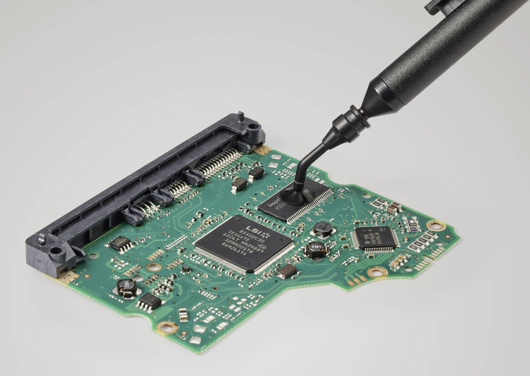 Eine grüne Leiterplatte mit elektronischen Bauteilen und einem schwarzen Werkzeug, das auf die Oberfläche aufgesetzt ist.