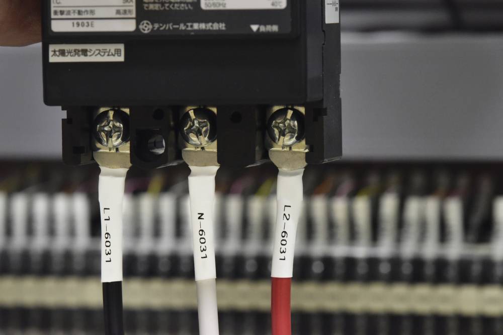 Drei beschriftete, farbige Kabel sind in einen Sicherungskasten eingesteckt. Beschriftungen lesen: L1-603, N-603, und L2-603.