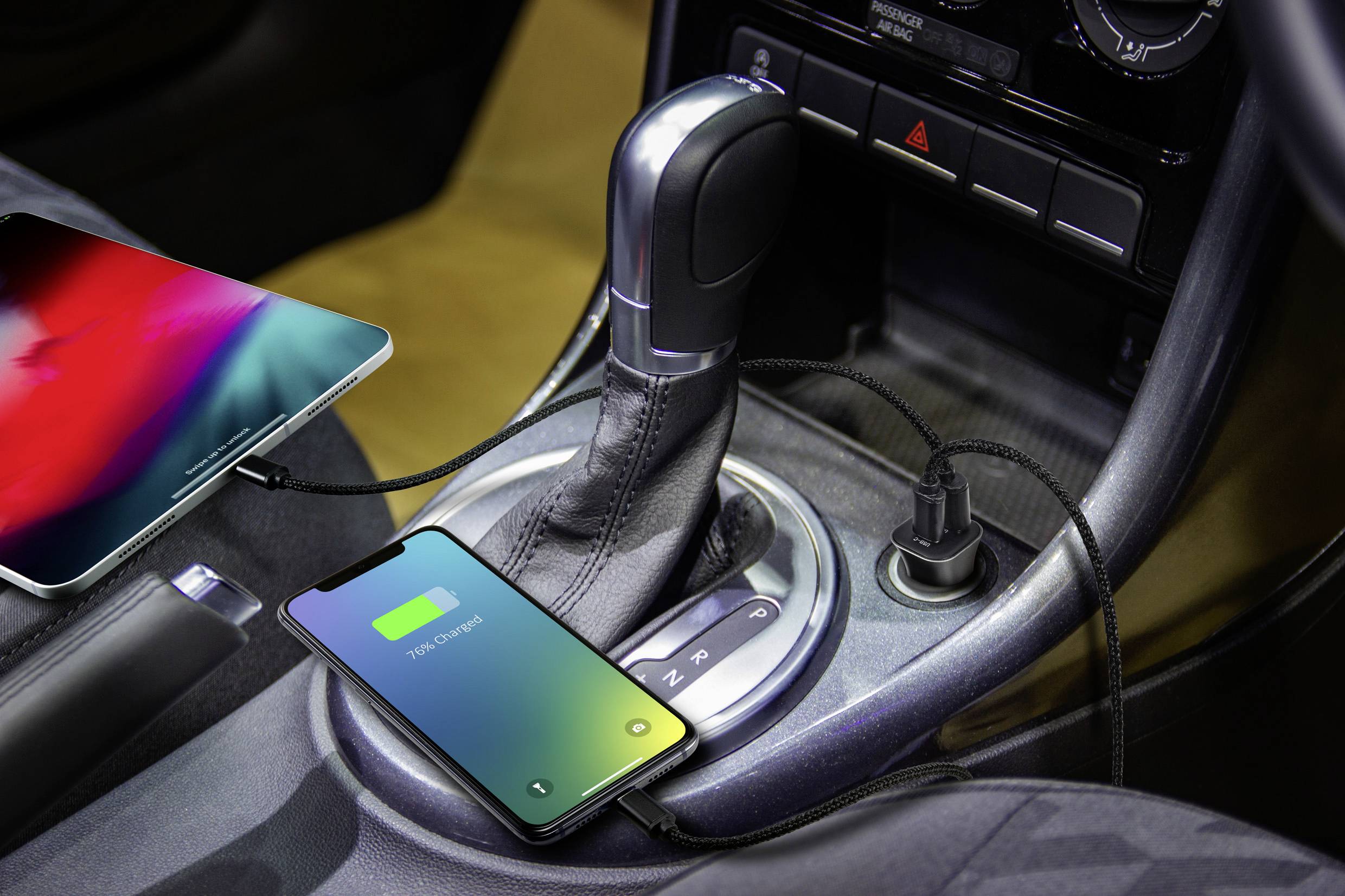 Ein Smartphone und ein Tablet sind im Auto angeschlossen und laden; das Display des Smartphones zeigt '100% geladen' an.