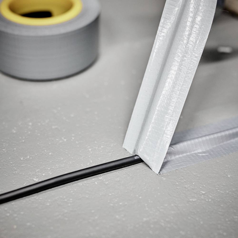 Ein Stromkabel wird mit grauem Klebeband am Boden befestigt, um es zu sichern und Stolperfallen zu vermeiden.