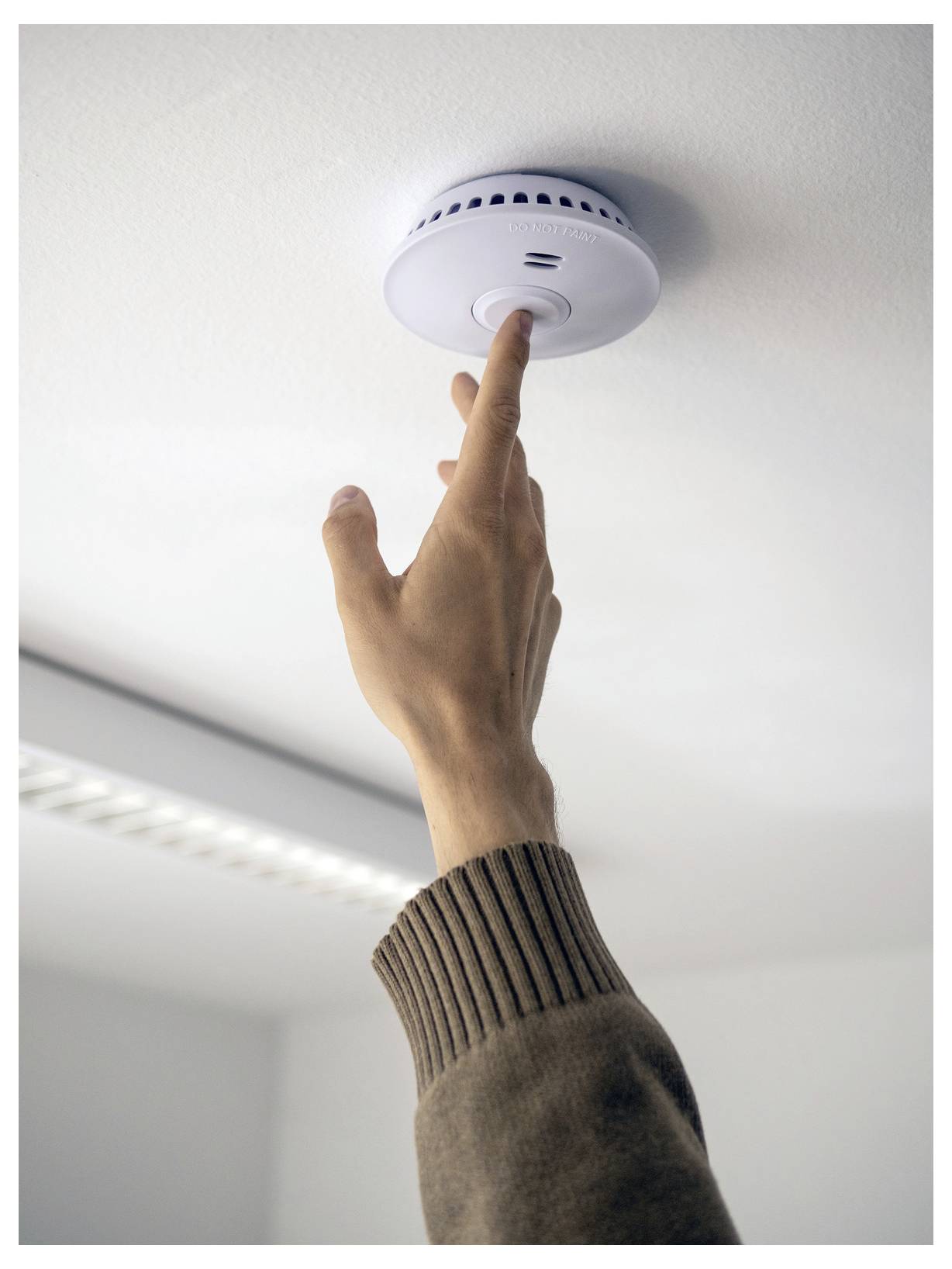 Person drückt auf die Testschaltfläche eines Rauchwarnmelders an der Decke.
