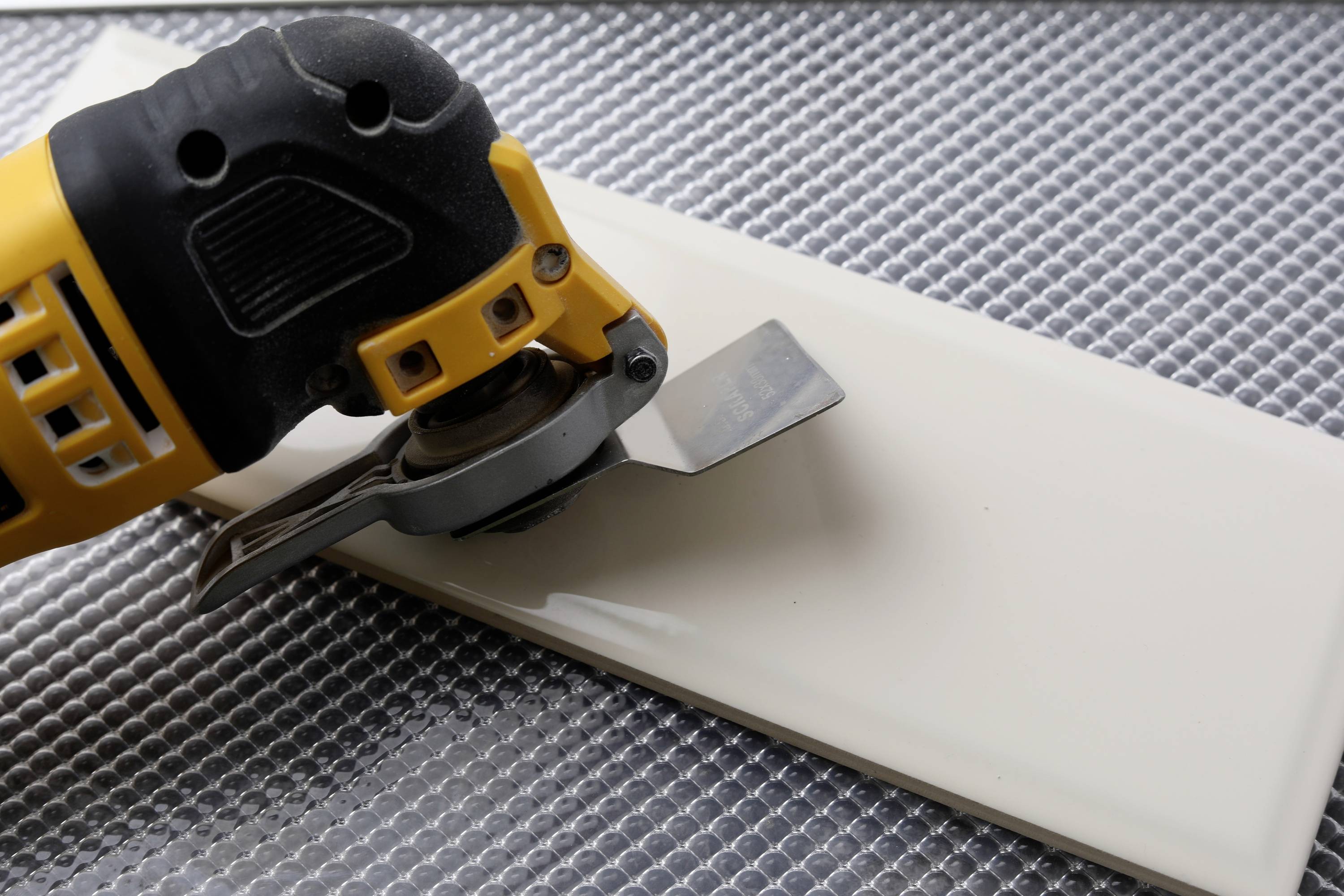 Eine elektrische Fliesenschneidmaschine schneidet eine weiße Keramikfliese auf einem strukturierten Untergrund.