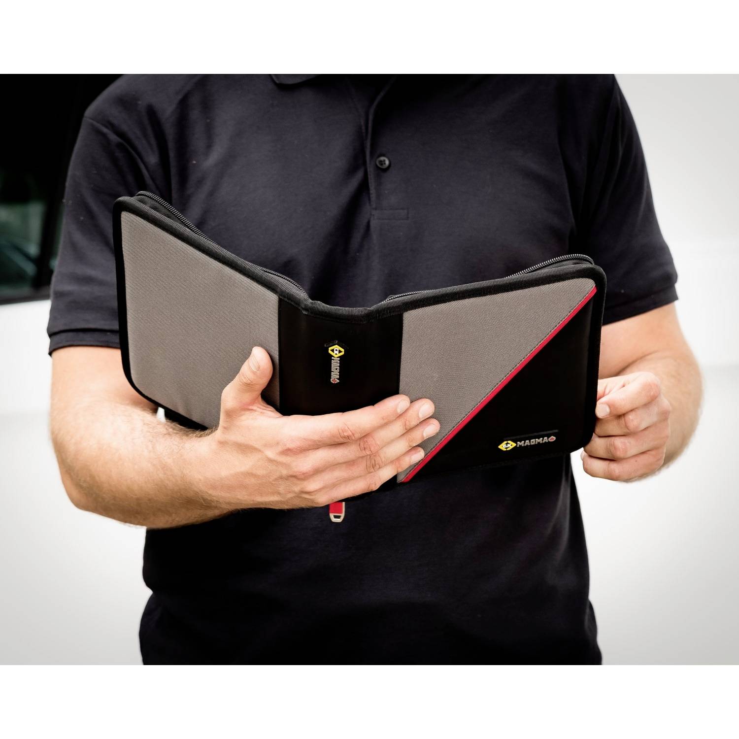 Eine Person hält eine schwarze Mappe mit grauem und rotem Detail in der Hand. Die Mappe hat das Logo 'Hama'.