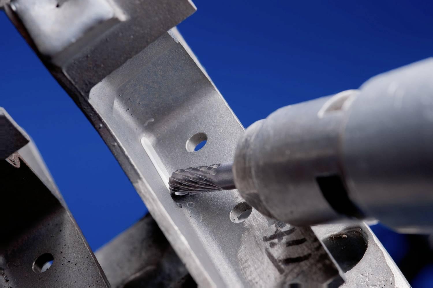 Nahaufnahme eines Bohrers, der ein Loch in ein metallisches Werkstück bohrt. Der Hintergrund ist blau.