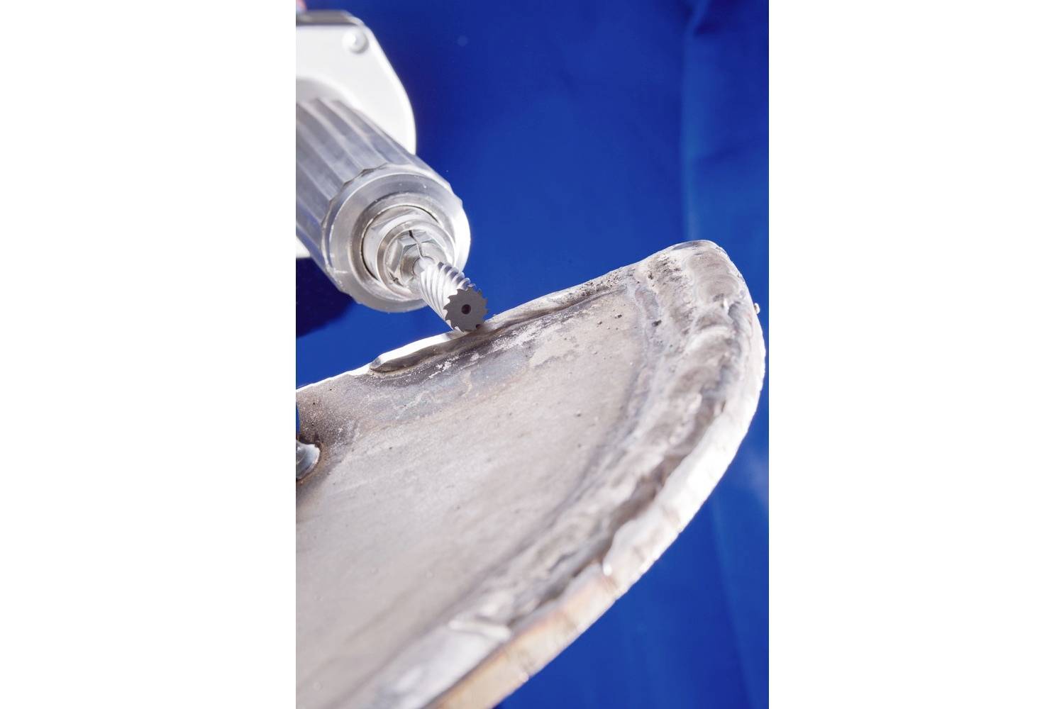 Ein Schleifgerät bearbeitet den Rand eines Metallstücks vor blauem Hintergrund.