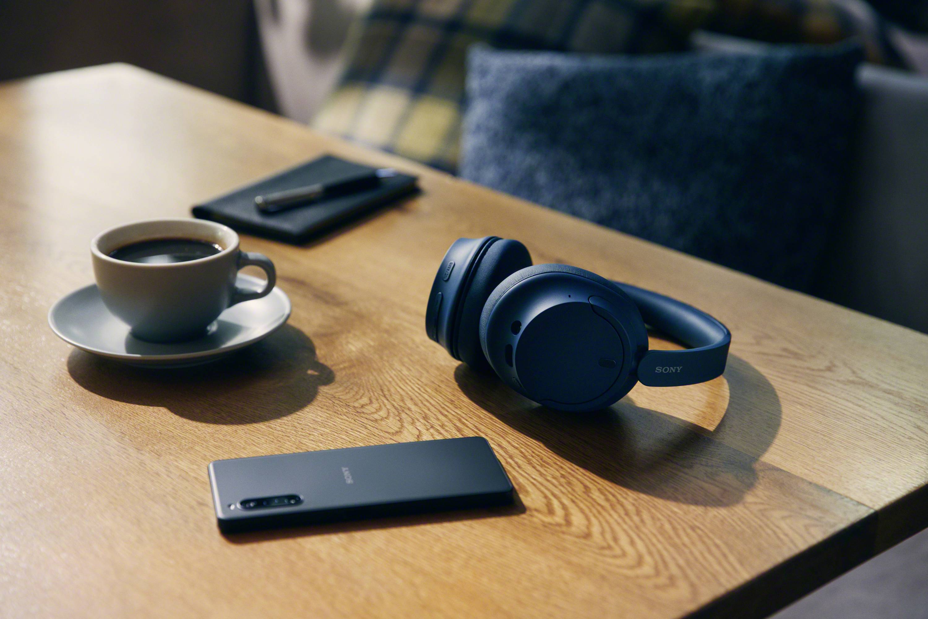Smartphone, Kopfhörer und Kaffeetasse auf Holztisch; ruhige Arbeitsumgebung.