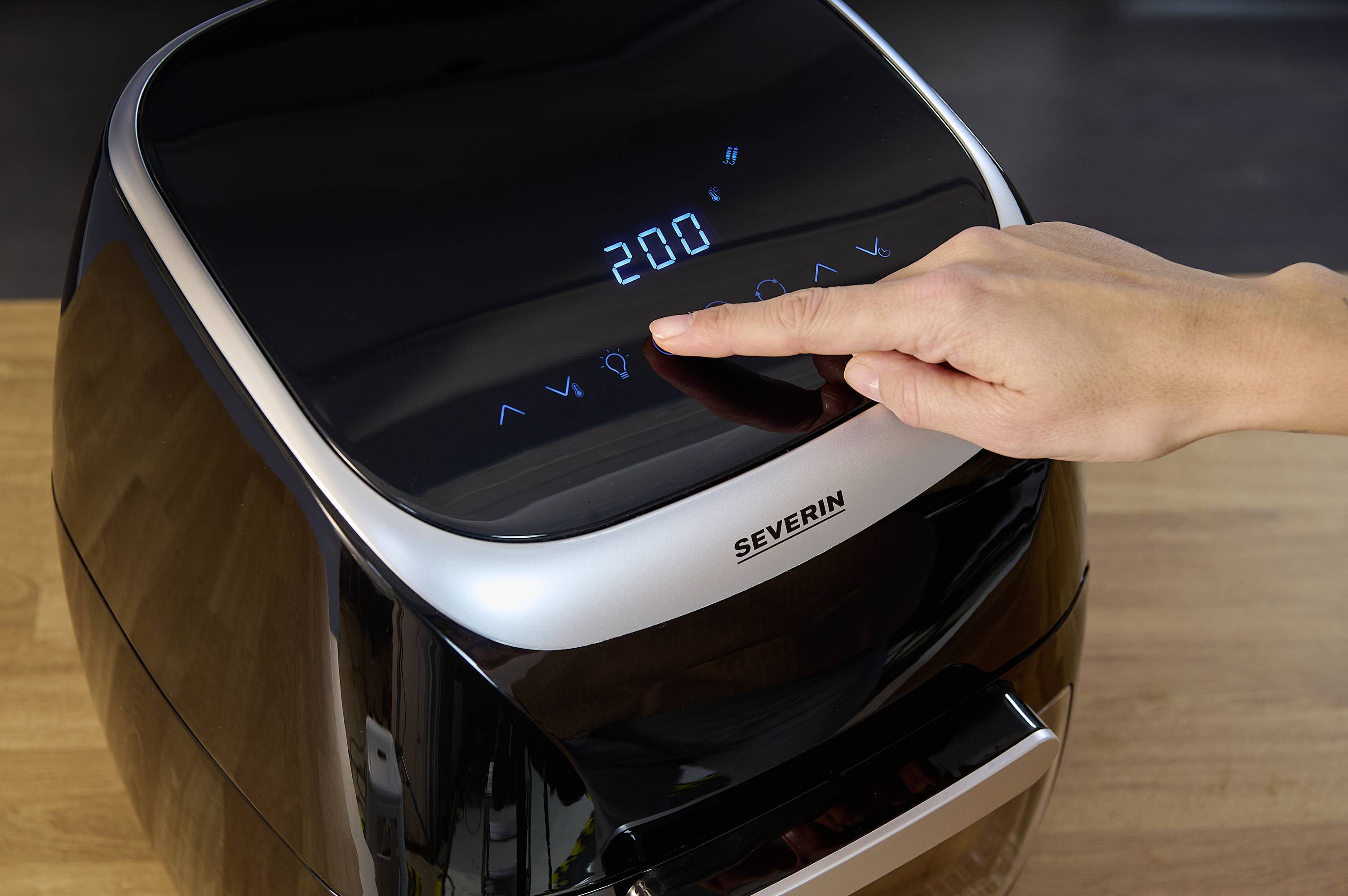 Eine Person bedient eine Heißluftfritteuse, indem sie die Temperatur von 200 Grad Celsius über ein digitales Display einstellt.