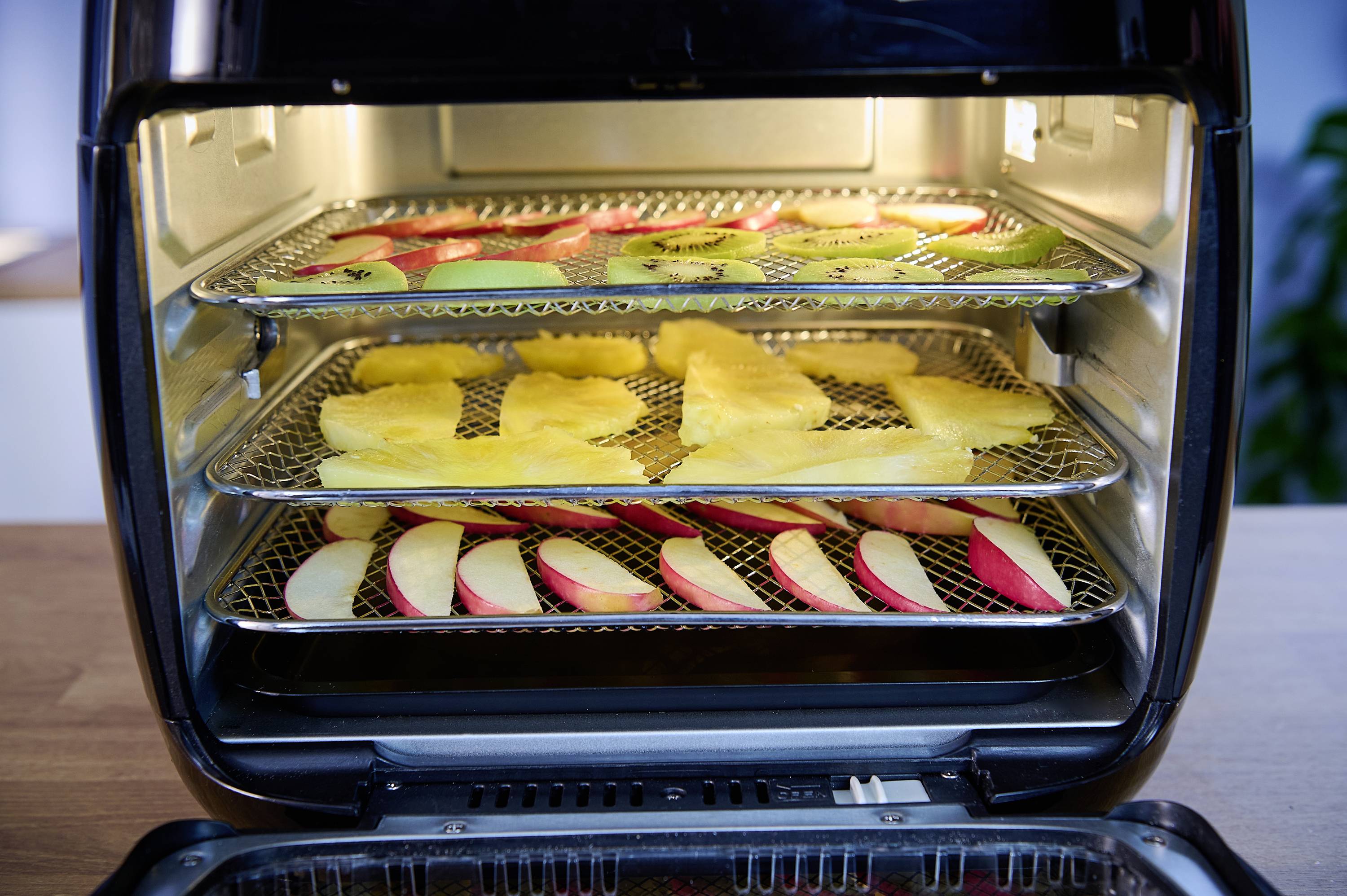 Ein geöffneter Ofen mit drei Einschüben. Oben sind Apfel- und Kiwi-Scheiben, in der Mitte Ananasscheiben, unten Apfelscheiben.