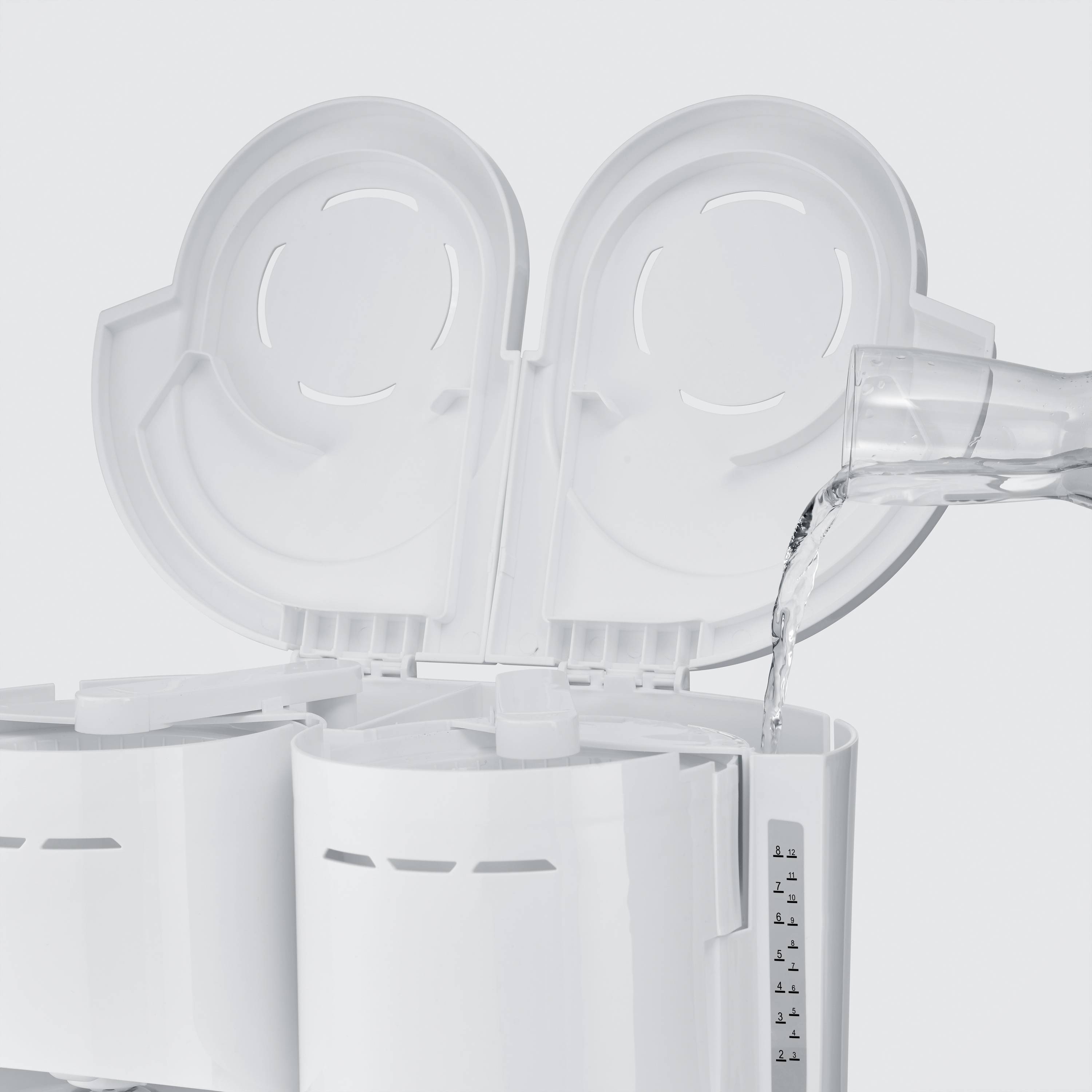 Ein Wasserkocher mit offenem Deckel, während Wasser aus einem Behälter hineingegossen wird. Der Wasserstandsanzeiger ist sichtbar.