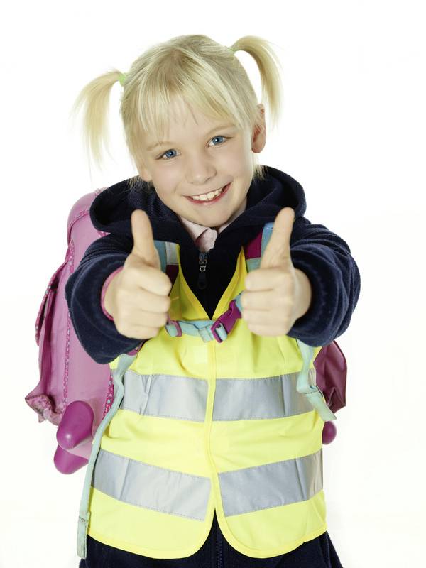Ein blondes Kind lächelt und zeigt mit beiden Daumen nach oben. Es trägt eine gelbe Warnweste und hat einen rosa Rucksack.
