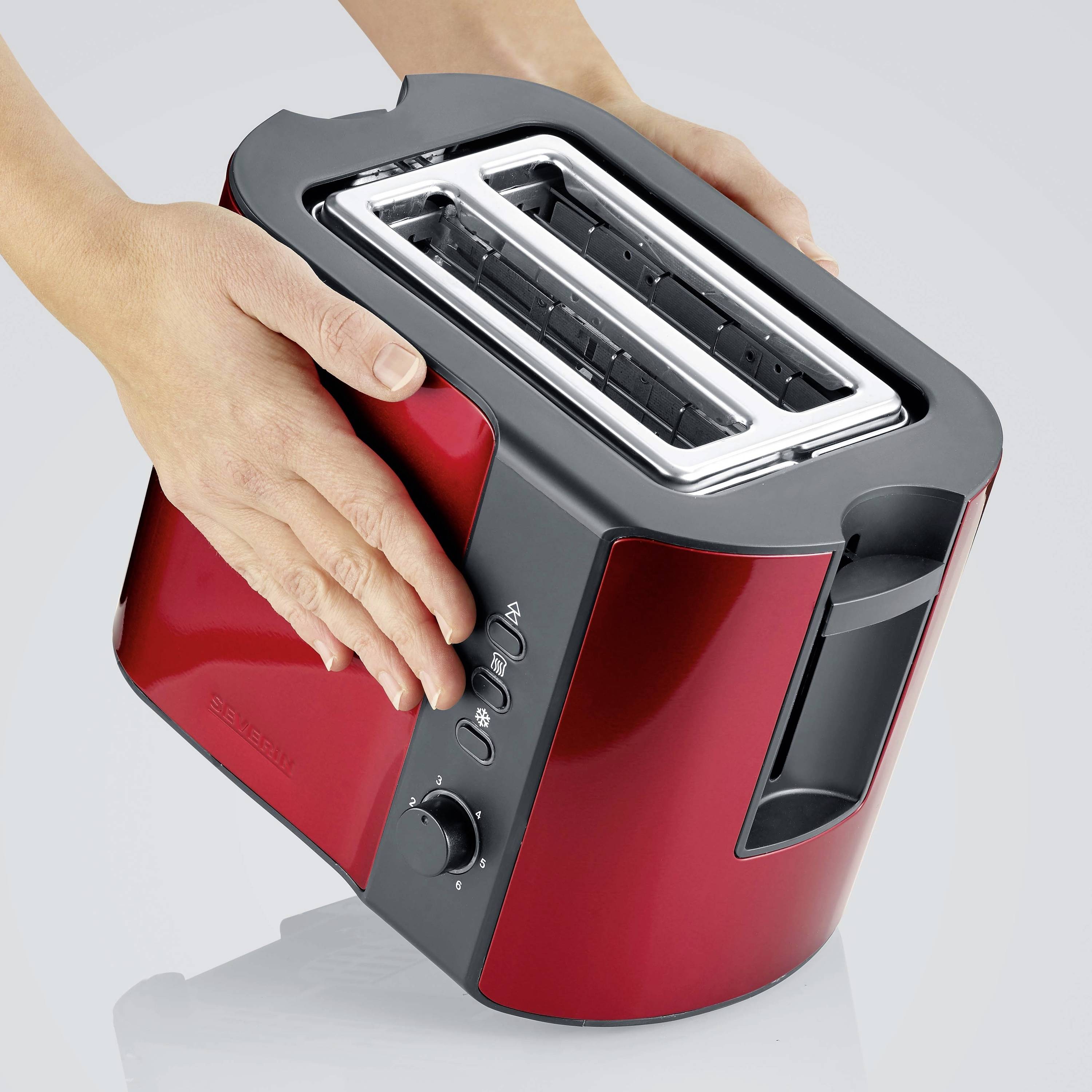 Eine rote Toaster wird von zwei Händen bedient. Der Toaster hat zwei Schlitze und Bedienelemente an der Seite.