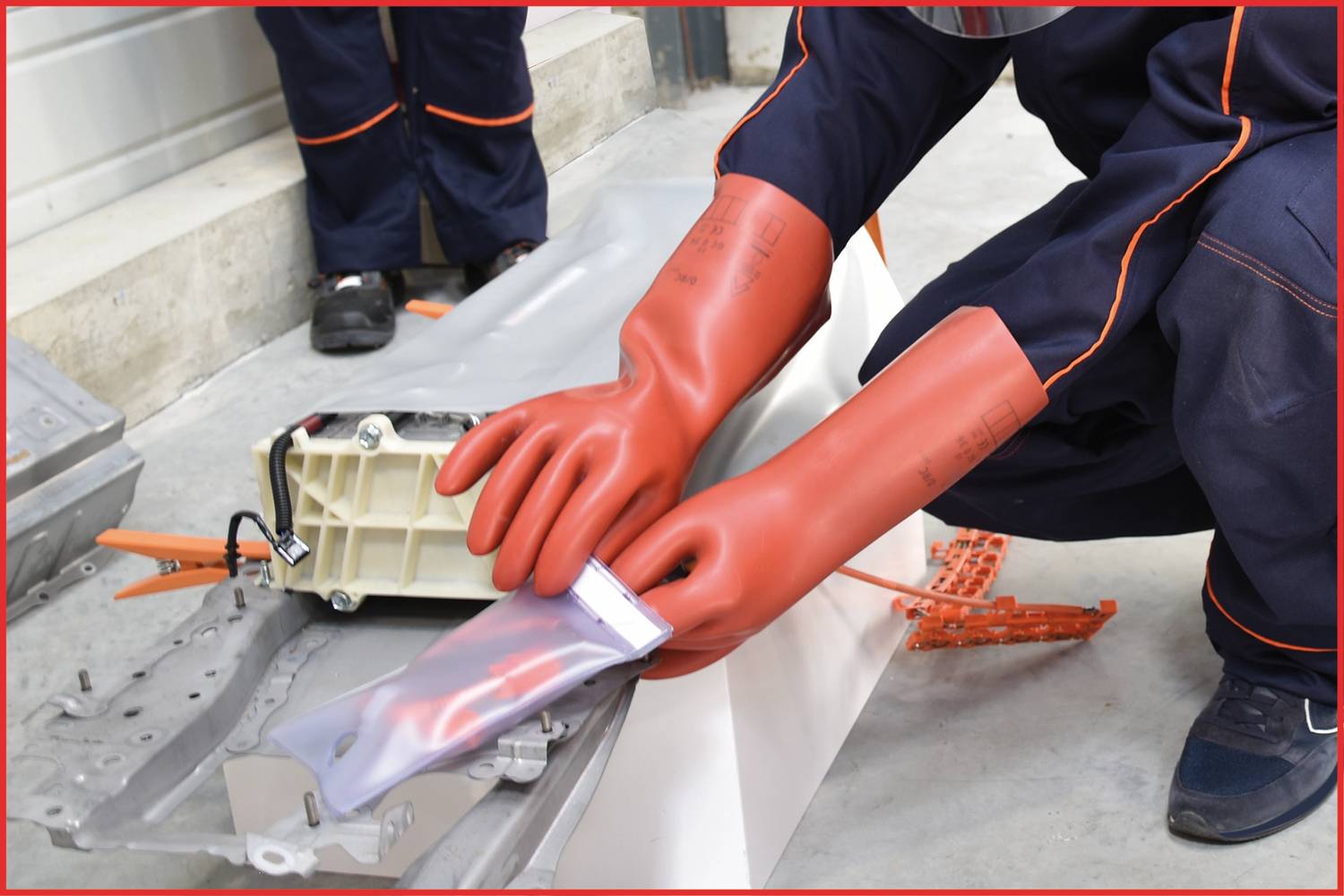 Person in Schutzkleidung und roten Handschuhen hantiert mit Elektrobatterie und Isoliermaterial. Sicherheit bei der Arbeit an Elektronik.