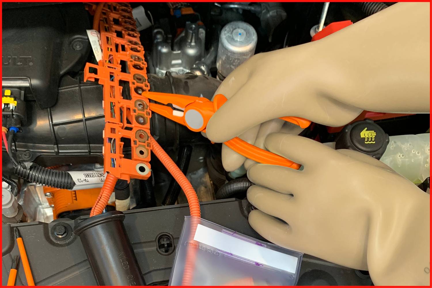 Person mit Gummihandschuhen arbeitet an einem elektrischen Bauteil in einem Auto. Nutzung einer Zange zur Kabelbearbeitung.