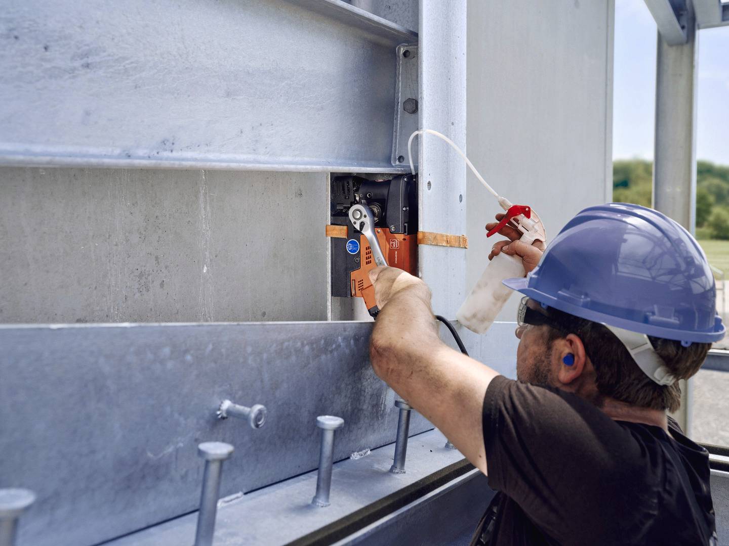 Ein Arbeiter mit Schutzhelm und Ohrstöpseln benutzt eine Zange, um an einer großen Metallstruktur zu arbeiten.