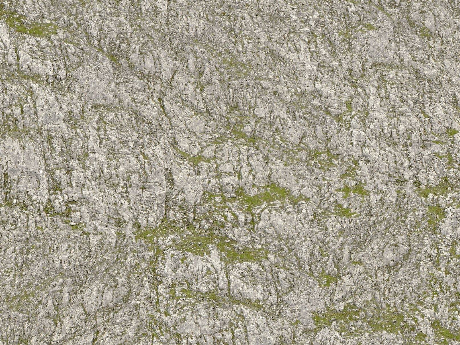 Raues Felsgestein mit vereinzelten Flechten und Moosbewuchs, zeigt eine natürliche, unregelmäßige Textur in grauen und grünen Tönen.