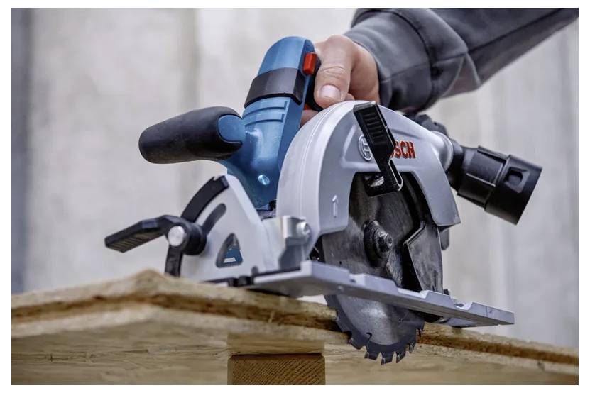 Eine Kreissäge, die durch eine Holzplanke schneidet, während eine Menschenhand das Werkzeug führt.