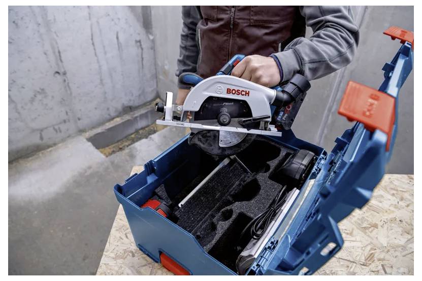 Eine Person, die eine Bosch-Kreissäge in eine blaue Aufbewahrungsbox mit maßgefertigten Schaumstoffeinsätzen auf einer Holzoberfläche vor einem Betonwandhintergrund platziert.