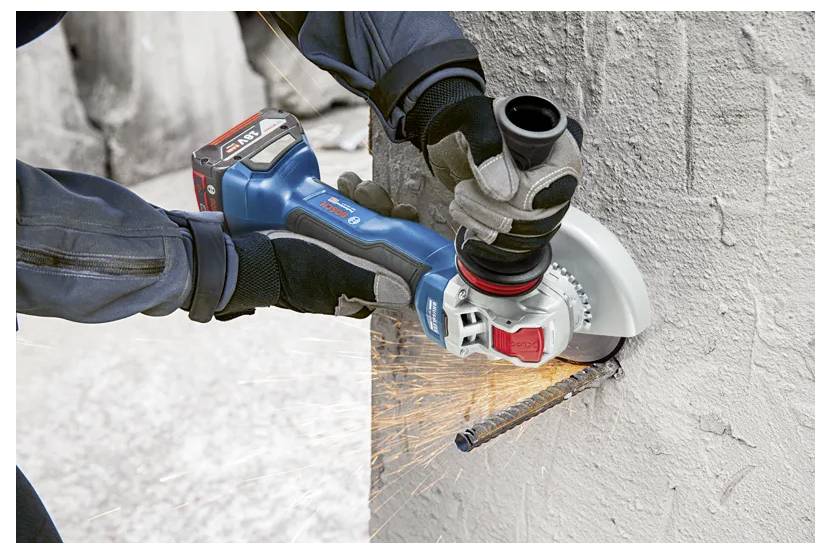 Eine Person benutzt einen blauen tragbaren Elektroschleiffer, um eine Metallbewehrung zu durchtrennen, die aus einer Betonwand herausragt, wobei Funken fliegen.