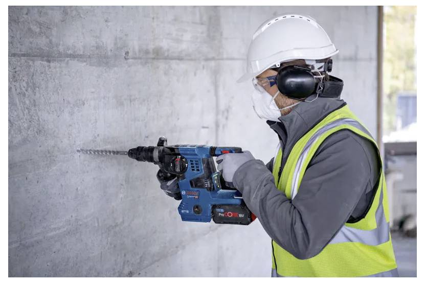 Ein Bauarbeiter in Sicherheitsausrüstung benutzt einen Bohrhammer an einer Betonwand.