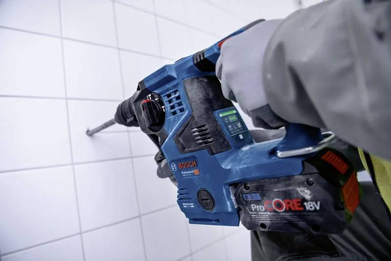 Eine Person mit Handschuh verwendet ein Bosch ProCORE 18V Elektrowerkzeug, um in eine geflieste Wand zu bohren und damit eine Heimwerker- oder Bauaufgabe zu verrichten.
