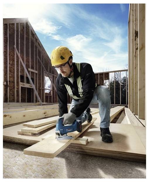 Ein Bauarbeiter mit Sicherheitsausrüstung verwendet eine Kreissäge, um Holzbretter an einer Baustelle unter einem klaren Himmel zu schneiden.