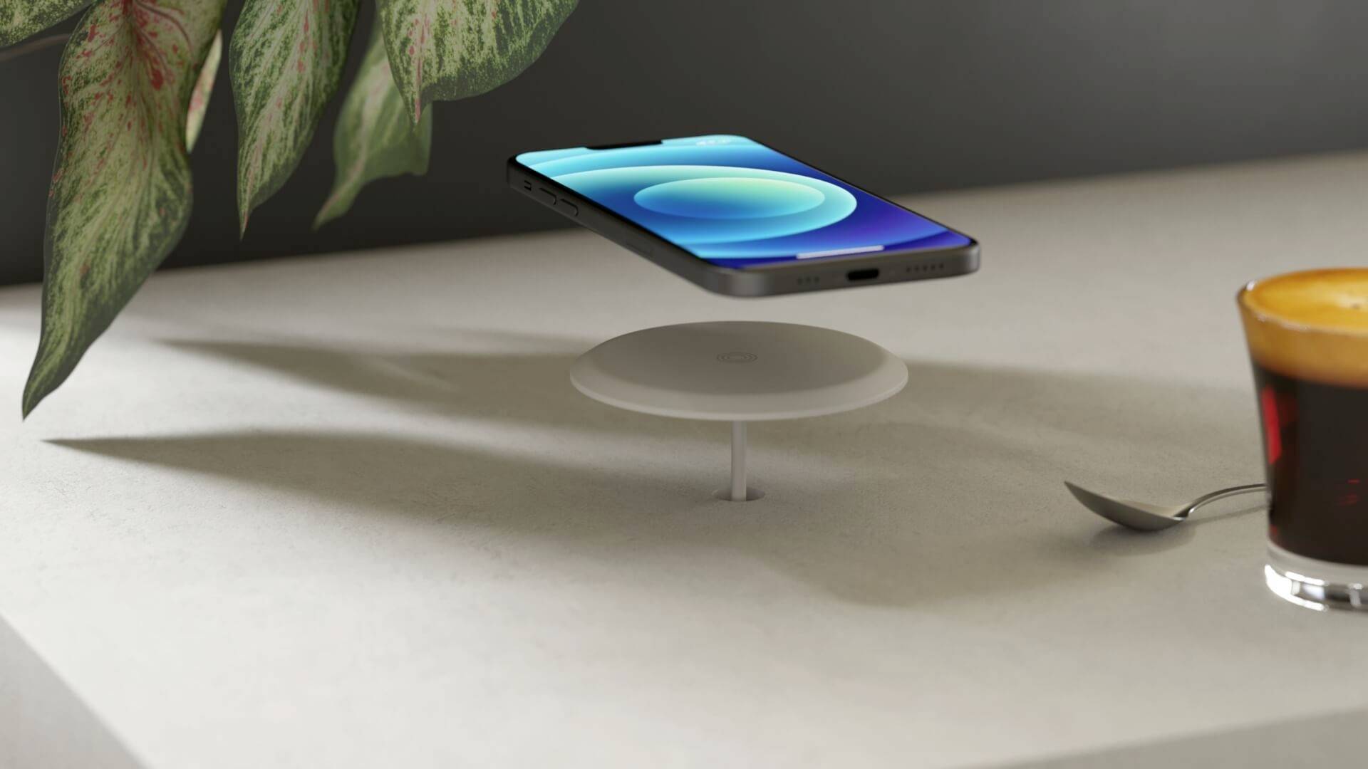 Ein Smartphone schwebt über einem runden, weißen Ladegerät auf einem Tisch. Daneben steht eine Espressotasse und liegt ein Löffel.