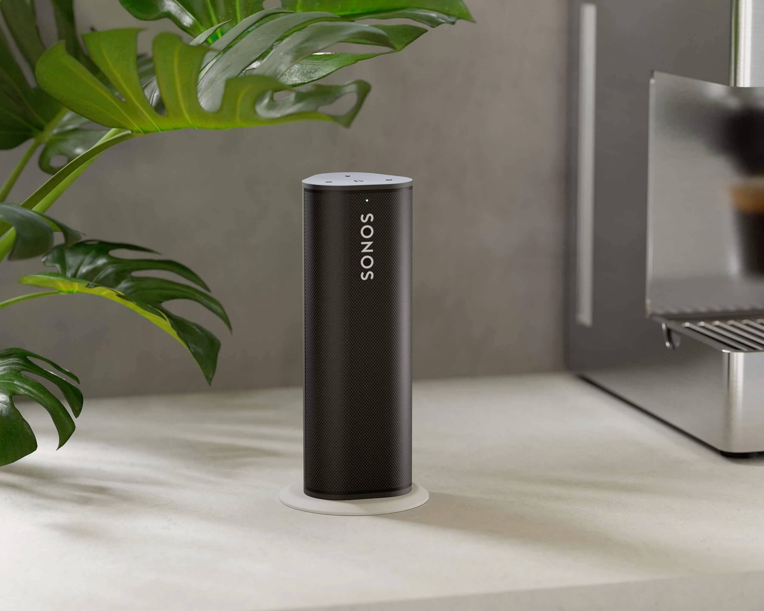 Ein schwarzer, zylindrischer Sonos-Lautsprecher steht auf einer hellen Arbeitsfläche neben einer Pflanze und einer Küchenmaschine.
