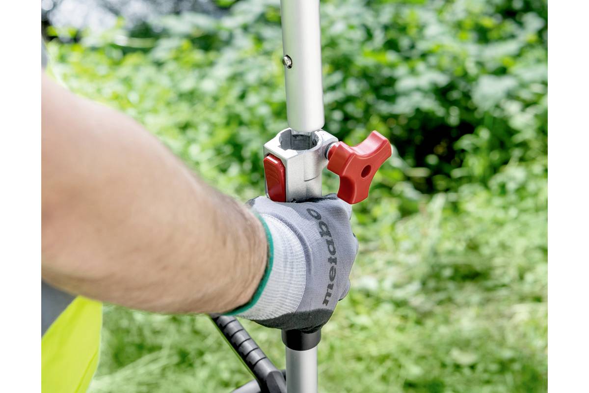 Eine Hand mit Handschuh justiert einen roten Griff an einer Metallstange vor grünem Hintergrund.