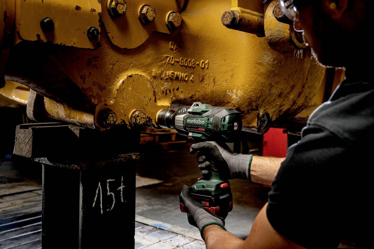 Eine Person repariert mit einem Akku-Bohrschrauber eine Industriemaschine.