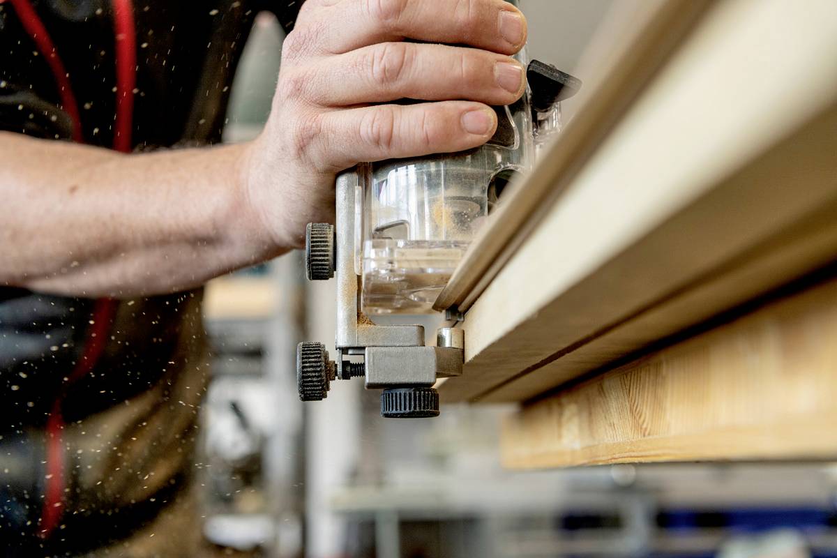 Eine Person arbeitet mit einer Holzbearbeitungsmaschine und glättet die Kante eines Holzbretts. Sägespäne fliegen in der Luft.