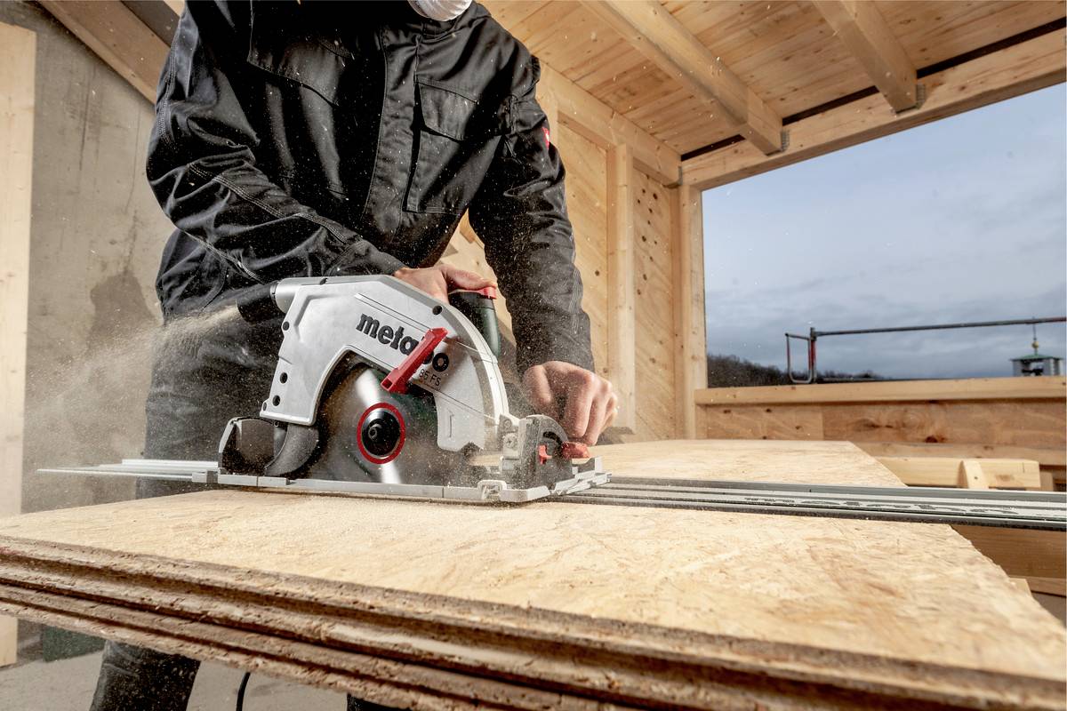 Arbeiter sägt Holzplatte mit einer Handkreissäge in einer Holzbaukonstruktion. Schutzkleidung wird getragen.