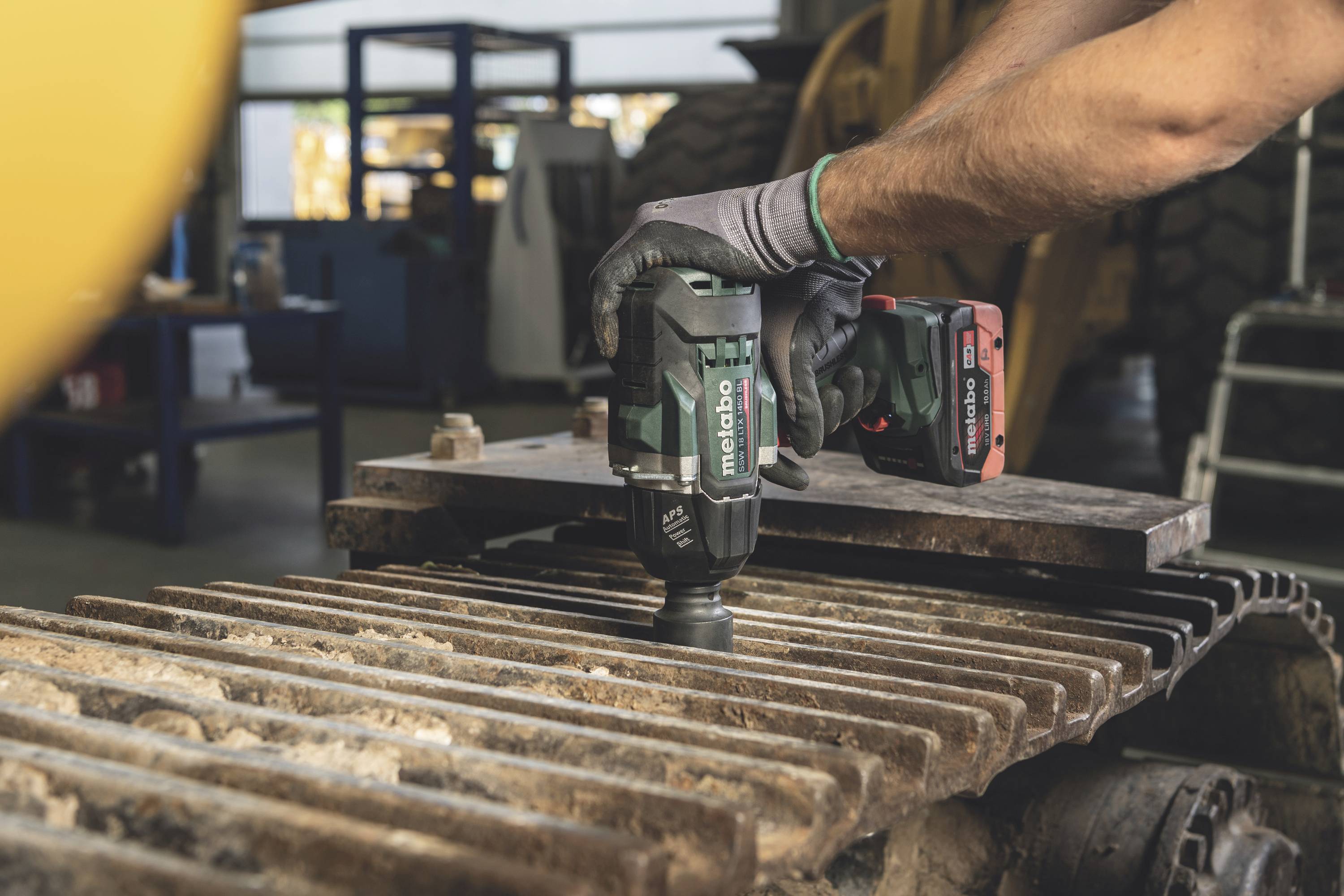 Eine Person verwendet ein elektrisches Werkzeug, um Metallteile auf einer Maschine in einer Werkstatt zu bearbeiten.