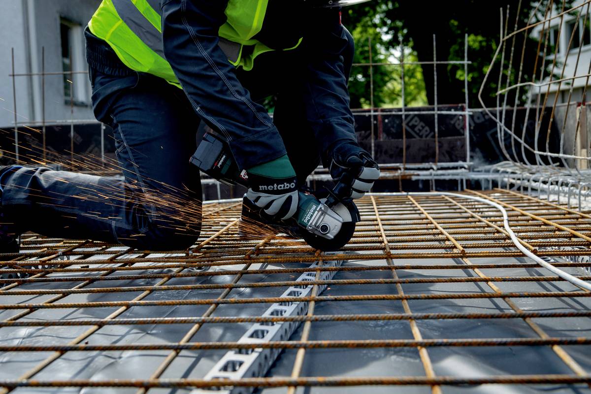 Eine Person schneidet Metallstäbe mit einem Winkelschleifer auf einer Baustelle. Funken sprühen, während Schutzkleidung getragen wird.