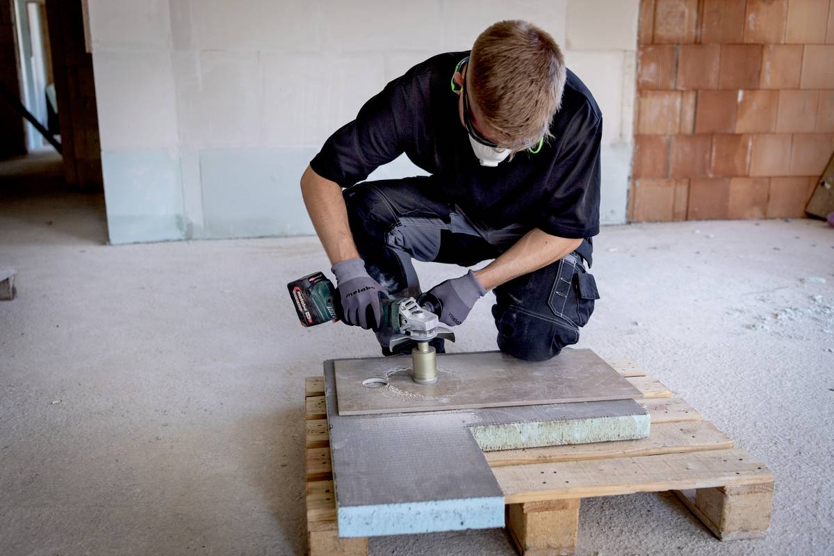 Ein Handwerker bearbeitet ein Stück Metall auf einer Palette. Er trägt Schutzbrille und Handschuhe und benutzt ein Elektrowerkzeug.