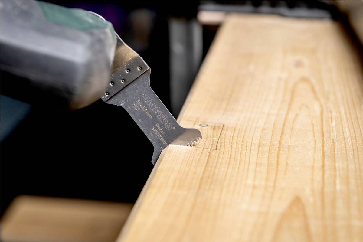 Eine oszillierende Säge schneidet in ein Stück Holz, zeigt präzises Arbeiten an einem Projekt in einer Werkstattumgebung.
