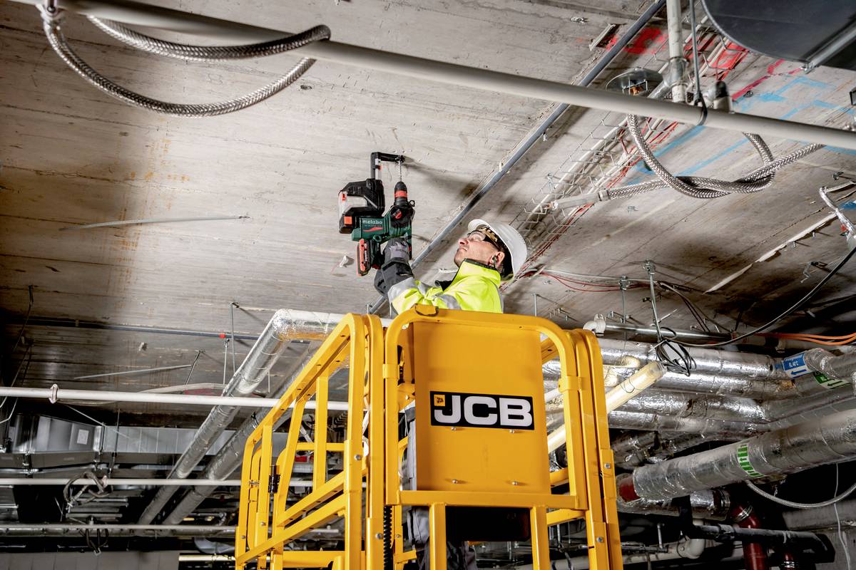 Arbeiter in Sicherheitskleidung steht auf einem Geländer und bohrt in eine Decke auf einer Baustelle.