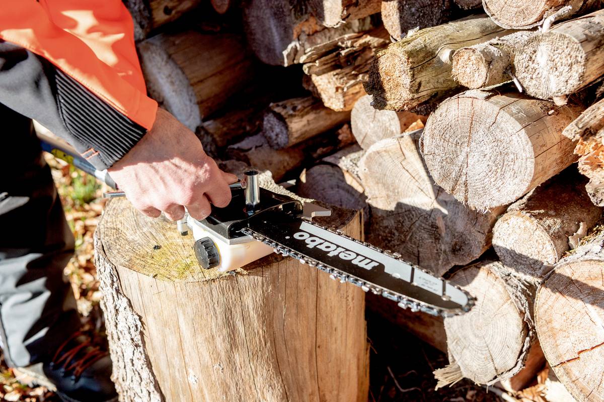 Eine Person schärft eine Kettensäge auf einem Baumstumpf vor einem Stapel Holzscheite.