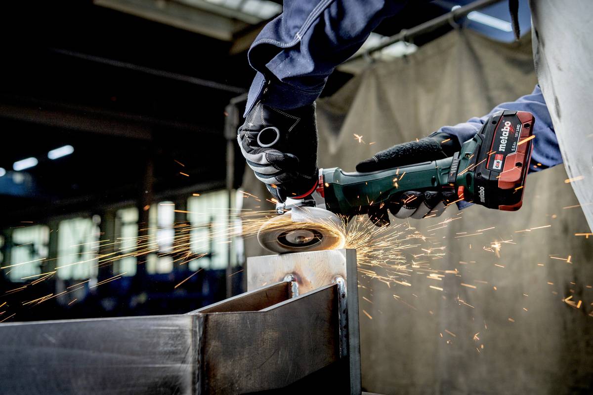 Eine Person schleift Metall mit einem Handschleifer. Funken fliegen von der Schleifscheibe. Die Umgebung wirkt industriell.