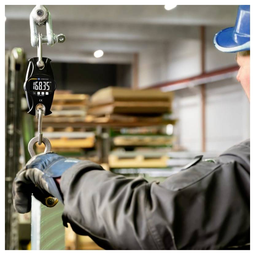 Ein Arbeiter mit Schutzhelm und Handschuhen hebt ein schweres Blech mit einem Kran an, während die Waage 168,35 anzeigt, in einer Industriewerkstatt.
