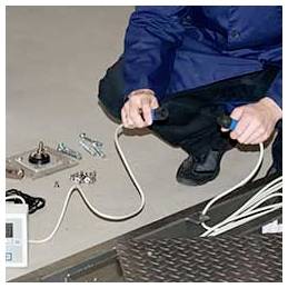 Person hockt sich neben einer Metallbodenöffnung hin, hält ein Elektrokabel und arbeitet mit Werkzeugen und Beschlägen auf dem Boden.