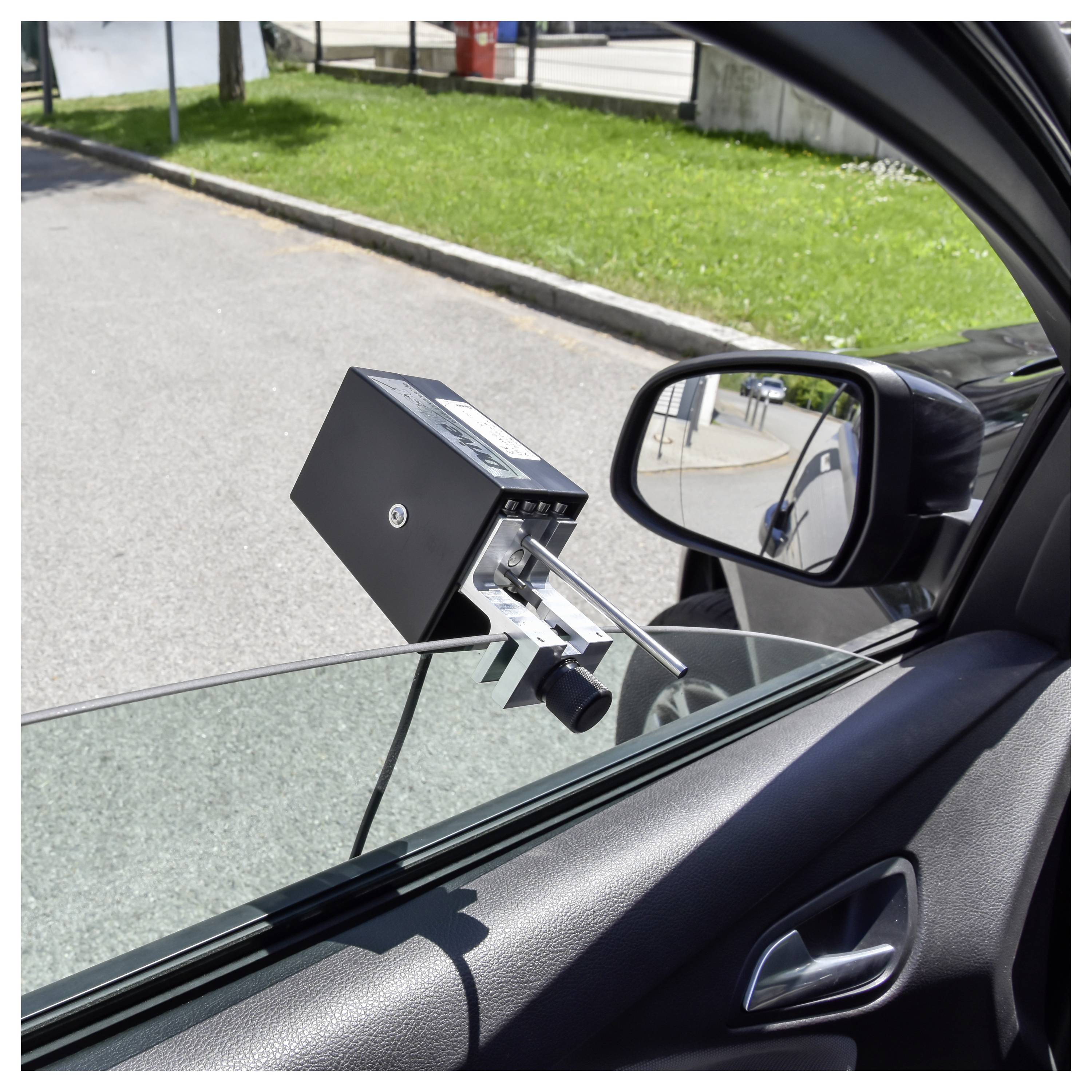 Ein schwarzes Straßenrandgerät, das in der Nähe eines Autofensters montiert ist, wahrscheinlich ein Maut- oder Parkplatzsensor, von innen aus dem Fahrzeug gesehen.