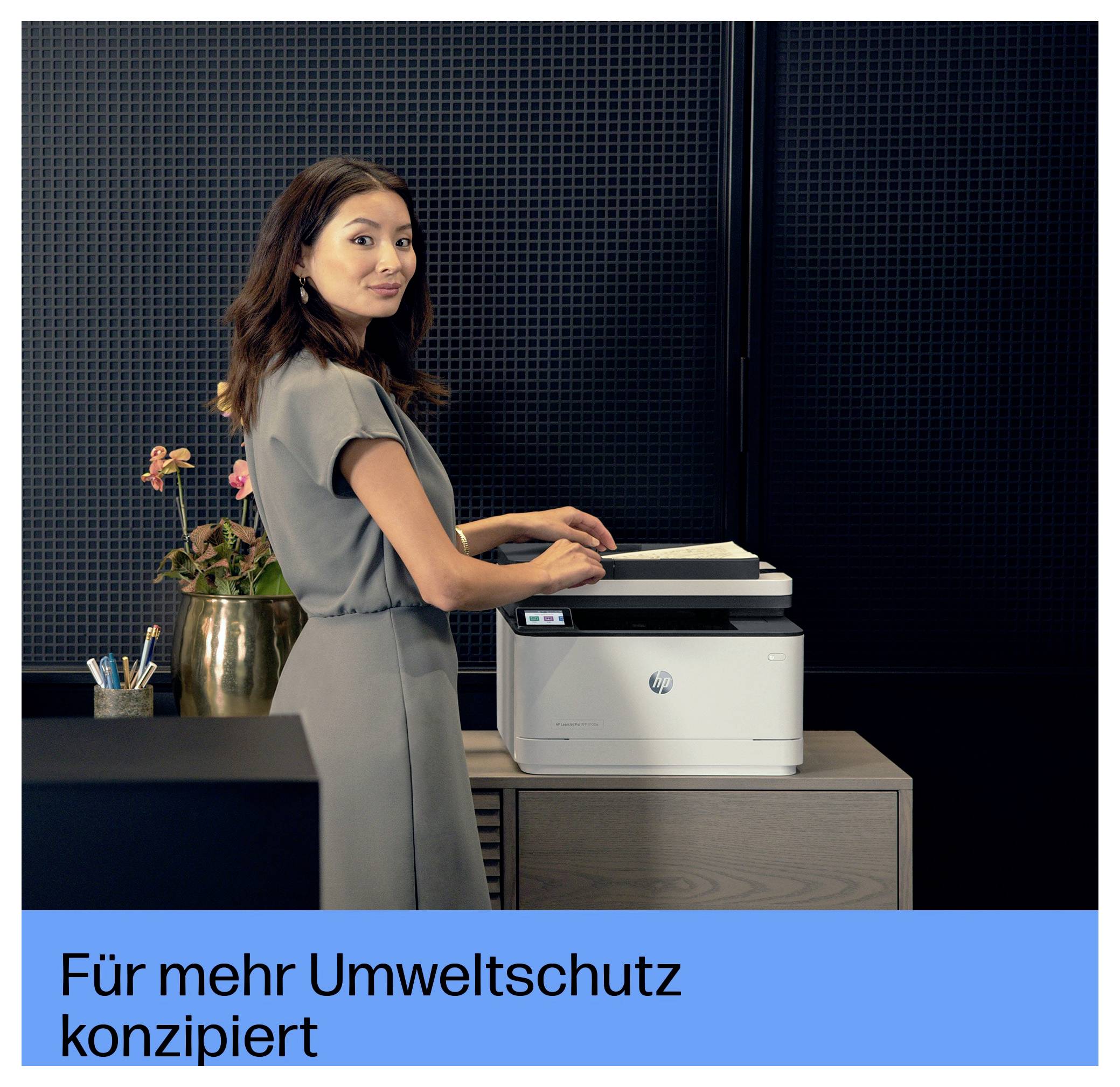 Frau, die einen HP-Drucker in einem Büro benutzt; deutscher Text lautet „Für mehr Umweltschutz konzipiert" („Designed for greater environmental protection").