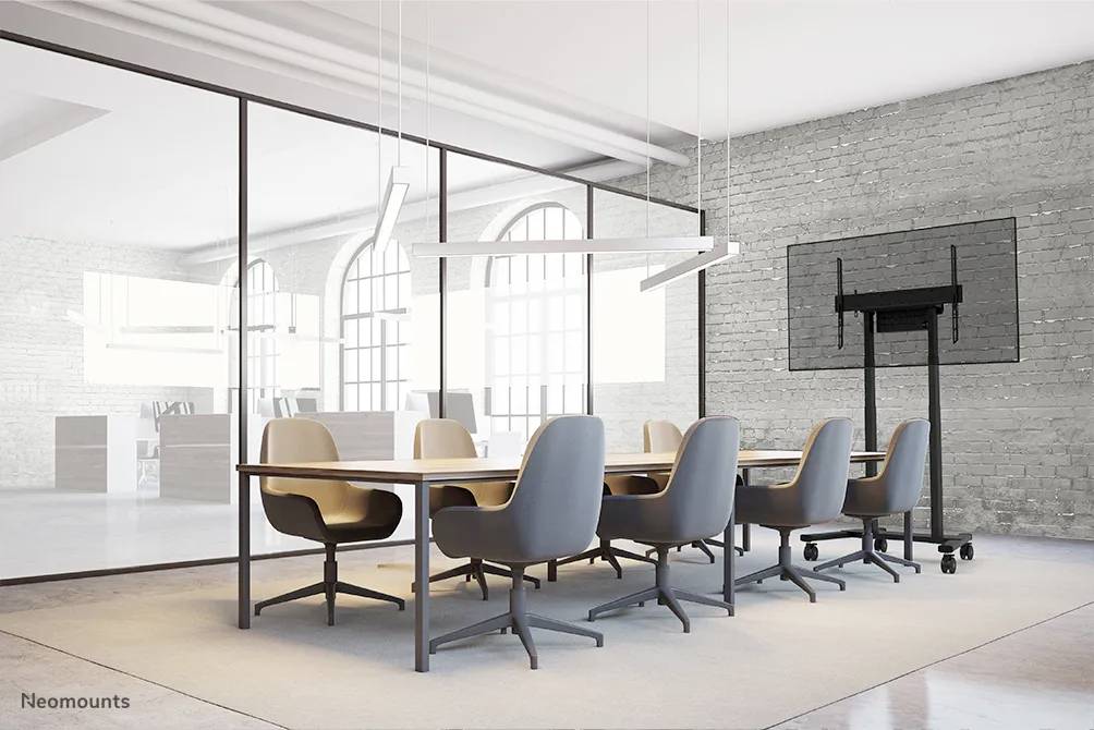 Ein moderner Konferenzraum mit einem großen Tisch, acht Stühlen, einem Flachbildschirm an der Wand und großen Fenstern im Hintergrund.