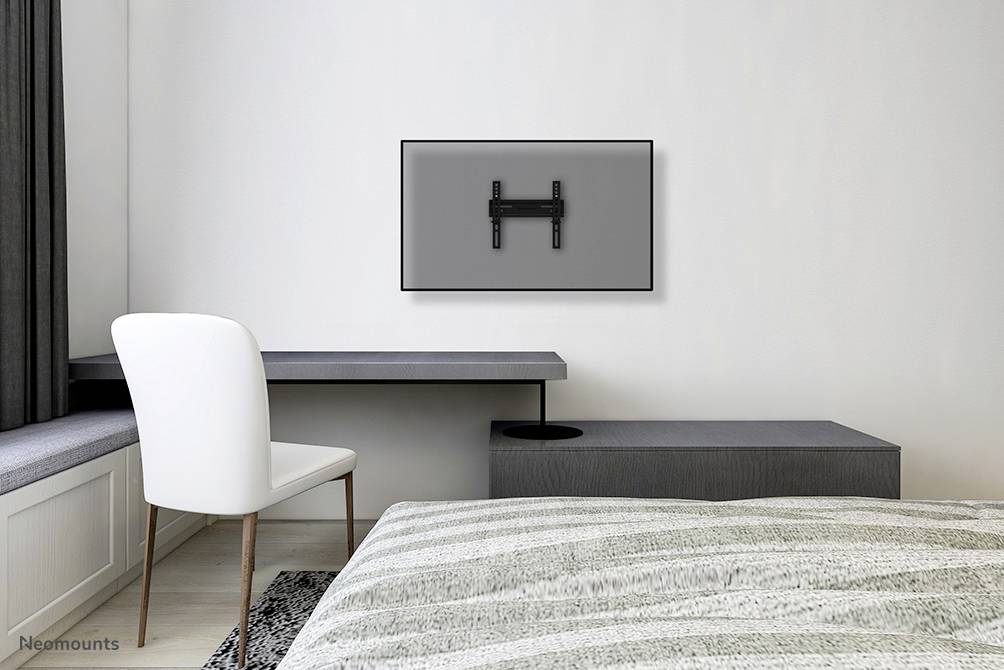 Ein leeres Fernsehhalterung an einer grauen Wand über einem minimalistischen Schreibtisch in einem modernen Schlafzimmer.