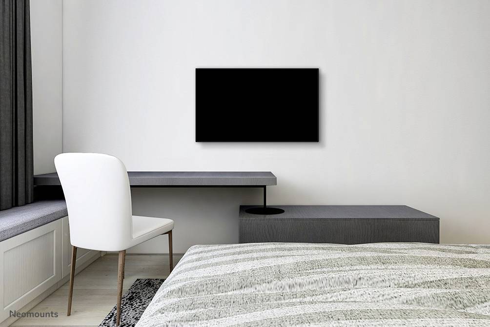 Ein minimalistisches Schlafzimmer mit einem Bett, einem Schreibtisch mit Stuhl am Fenster und einem schwarzen Fernseher an der Wand.