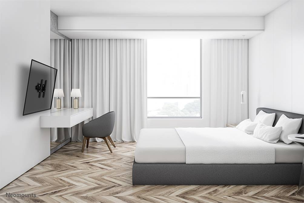 Ein modernes Schlafzimmer mit einem großen Bett, einem Schreibtisch und einem Stuhl. Ein großes Fenster bietet Tageslicht, Vorhänge daneben.