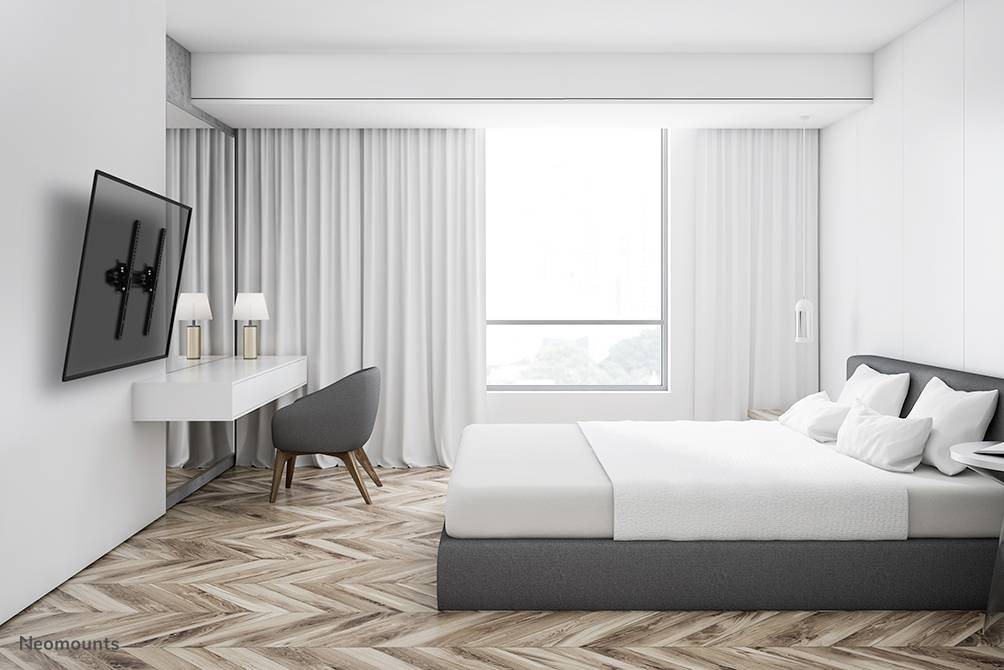 Helles, modernes Schlafzimmer mit Holzfußboden, grauem Bett, Schreibtisch, Stuhl und Wandfernseher, große Fenster bringen Tageslicht.