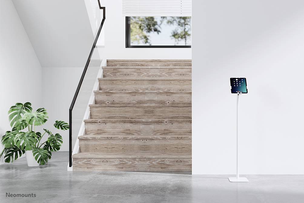 Treppenaufgang aus Holz mit schwarzem Geländer, daneben eine grüne Pflanze. Rechts steht ein Tablet auf einem weißen Ständer.