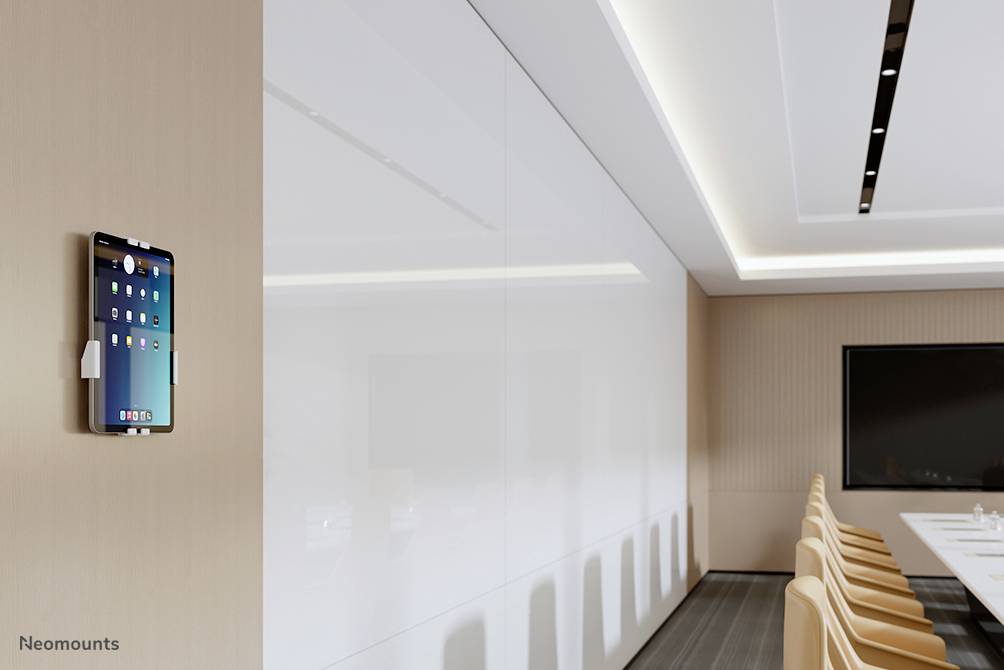Tablet an einer Wand in einem modernen Konferenzraum montiert, mit langen Tisch und weißen Wänden, links hängt ein Tablet.